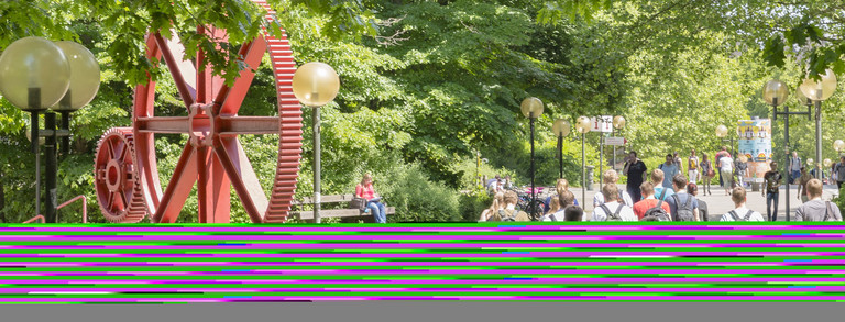 Header image students red gears campus north Students in summer on north campus, red gears in background.